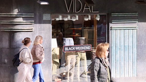 Dues dones passegen per Vic davant un aparador d'una botiga de roba que anuncia el Black Friday